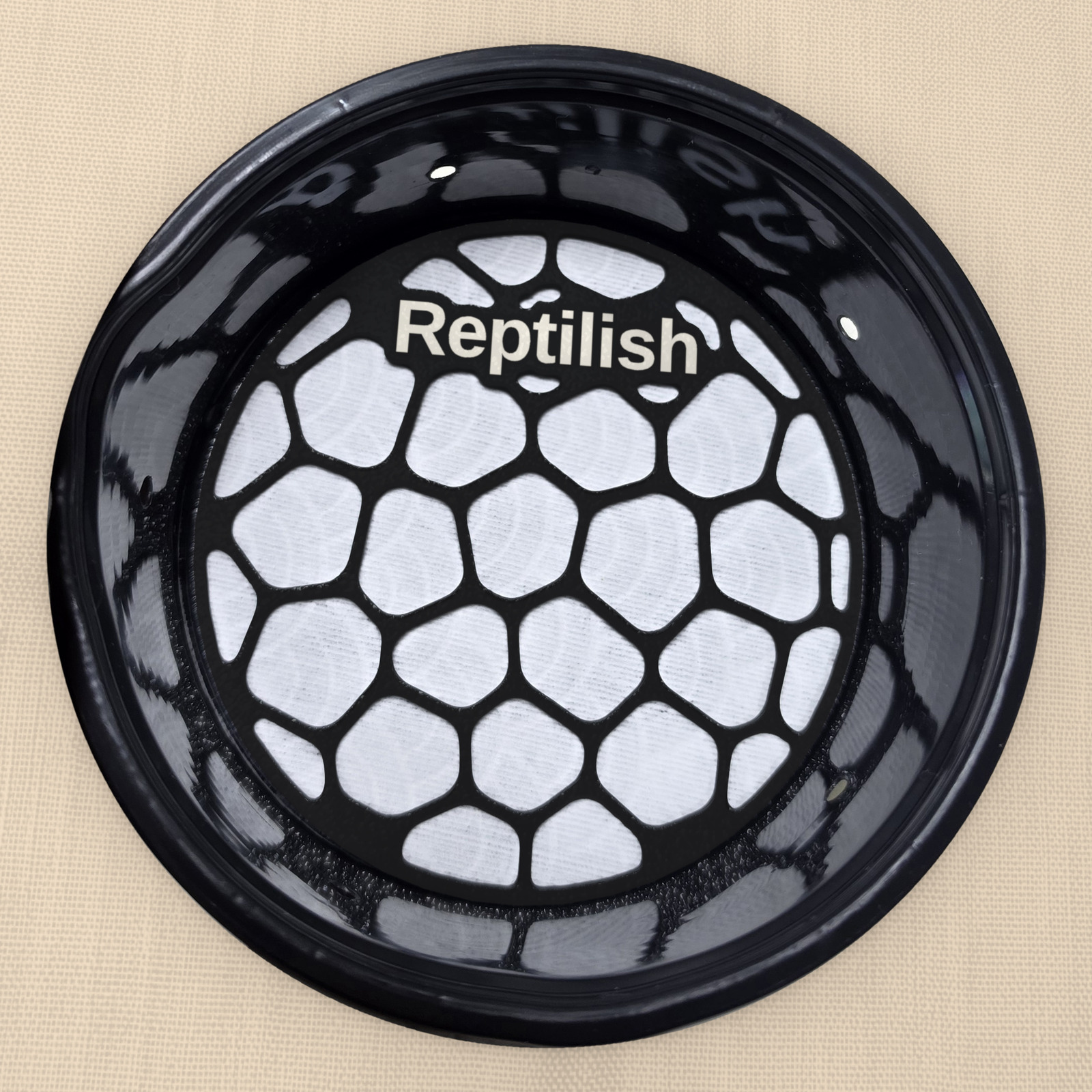 A round Carbon Black engraved Pebble Plate on the pad inside a deli cup